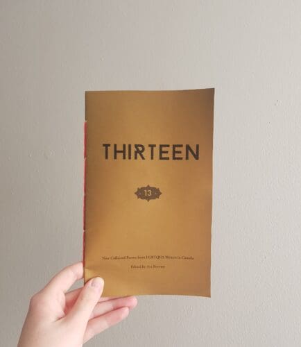 A hand holding a copy of Thirteen