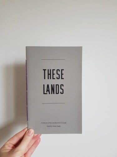A hand holding a copy of These Lands
