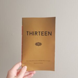 A hand holding a copy of Thirteen
